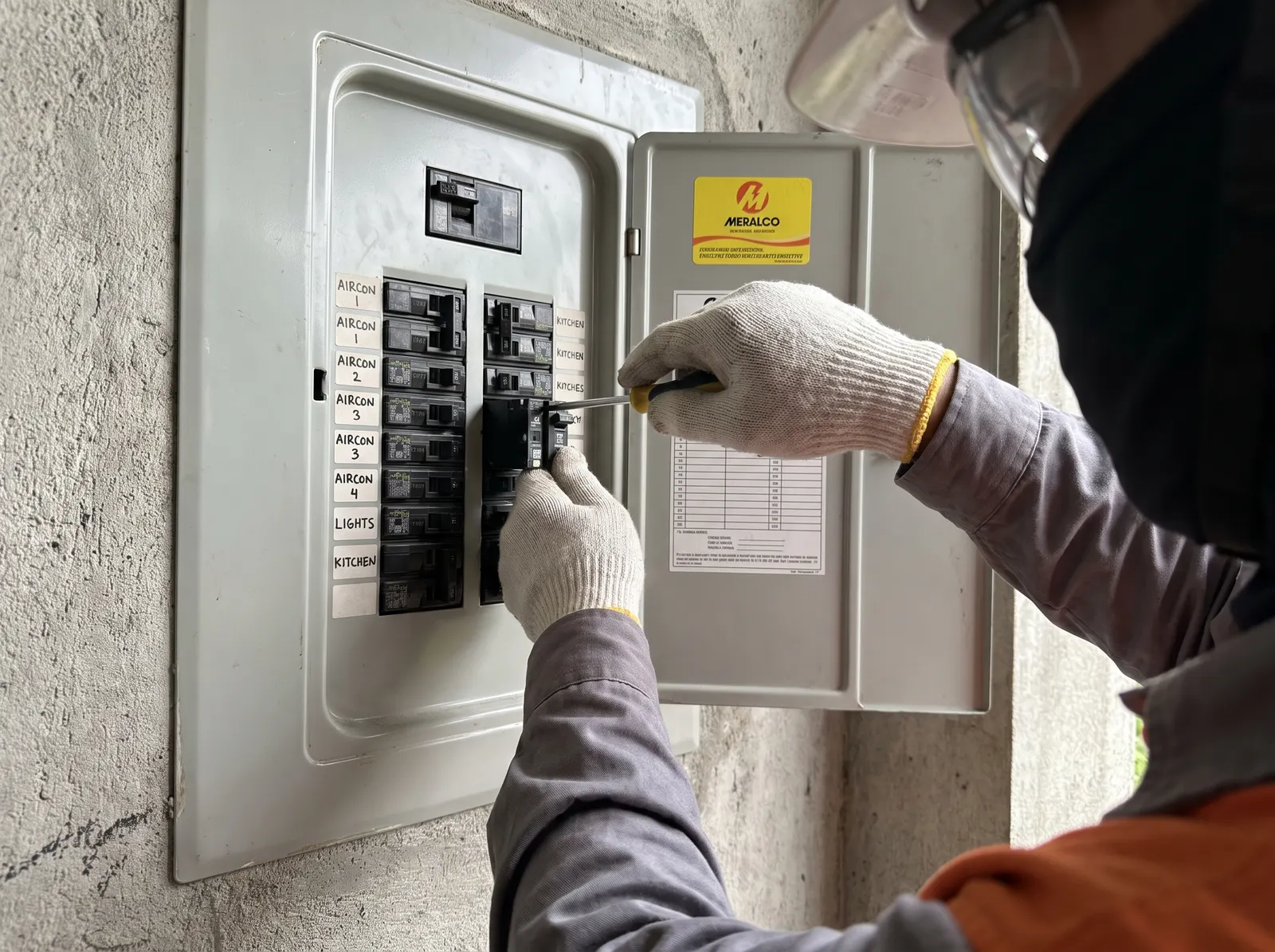 Electrician installing a circuit breaker into an open electrical panel, with rows of breakers and labeled circuits visible.